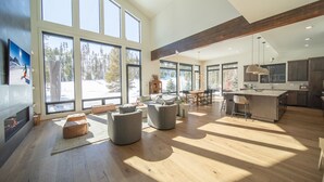 Amplia sala de estar con ventanas grandes, chimenea y cocina moderna.