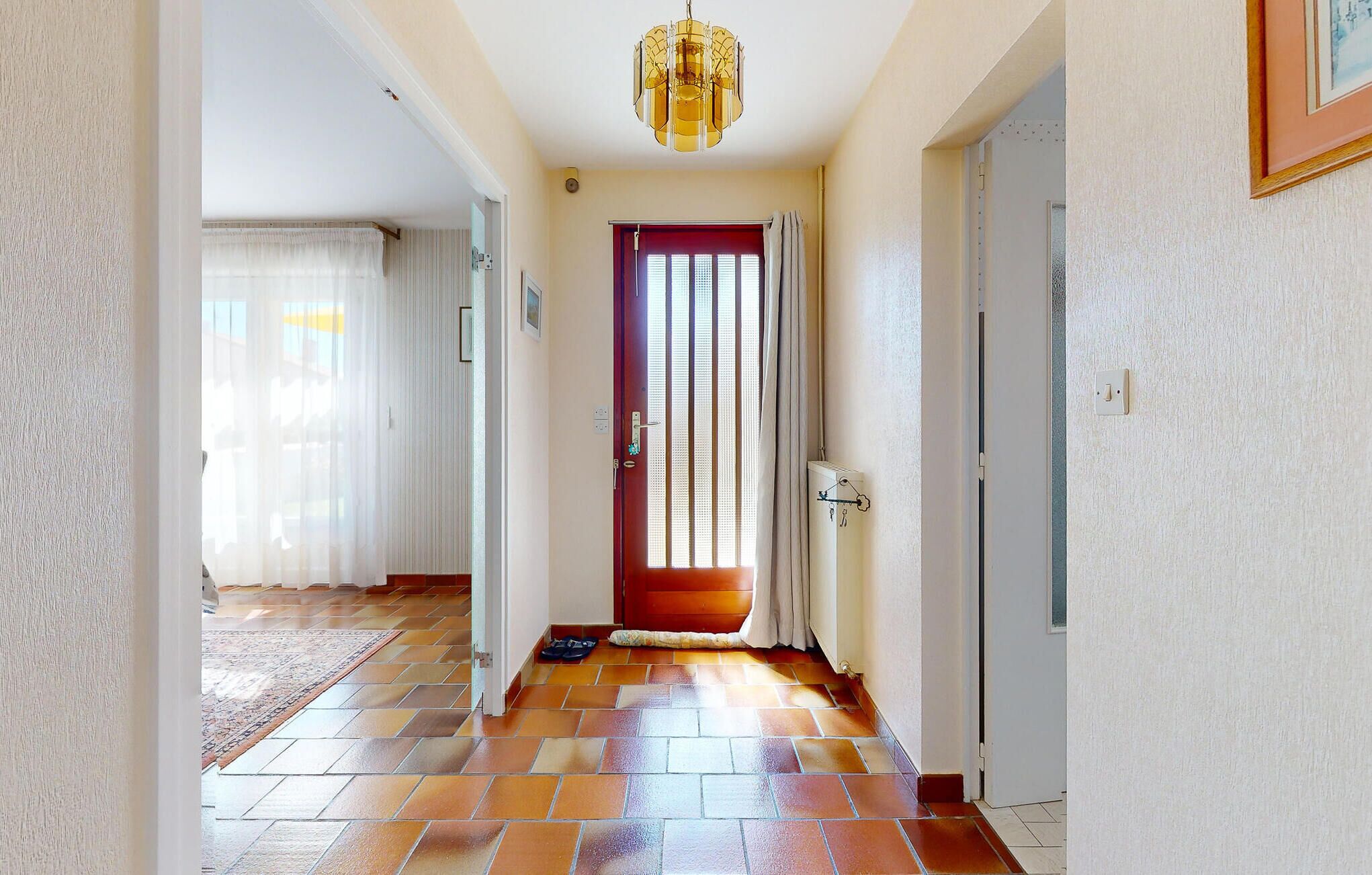 A hallway with a red door, a patterned rug, and a chandelier.