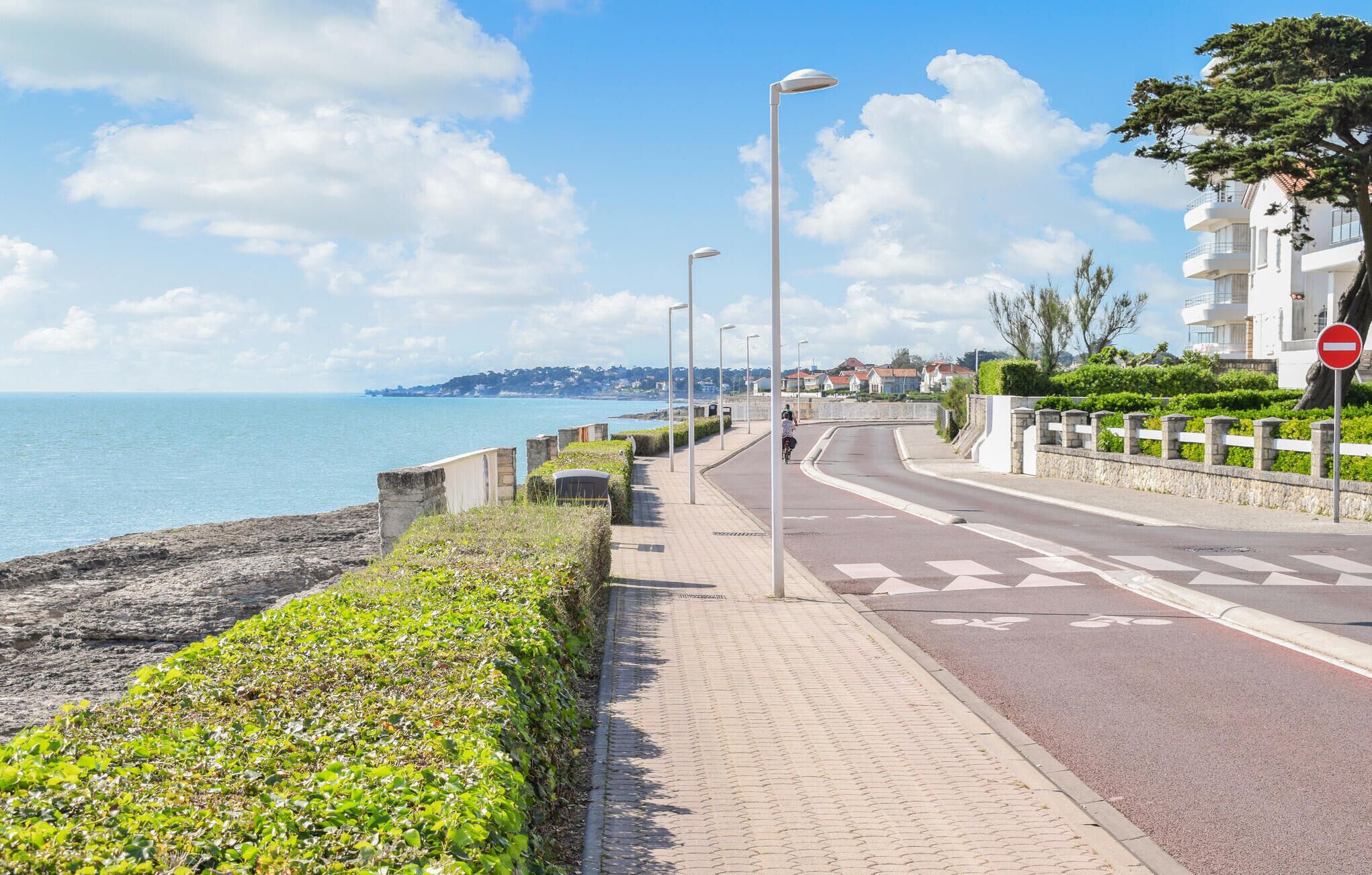 A coastal road with a pedestrian path, street lamps, and a no-entry sign.