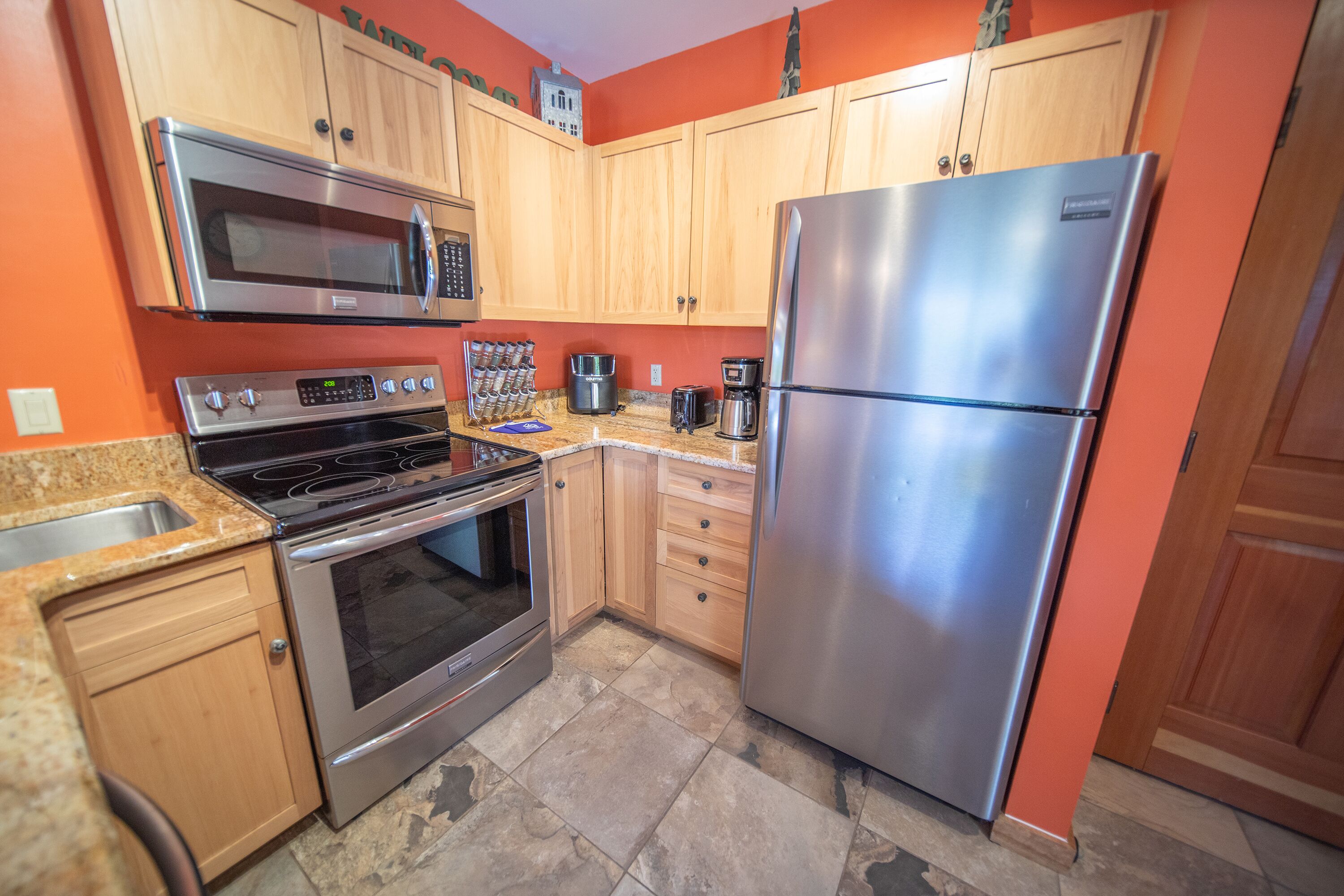 A kitchen with wooden cabinets, a stainless steel refrigerator, a microwave, a stove, and a coffee maker.