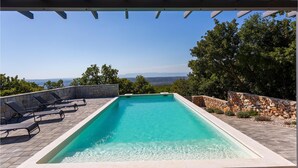 Une piscine rectangulaire à l’eau claire, entourée de murs de pierre et surmontée d’une pergola.