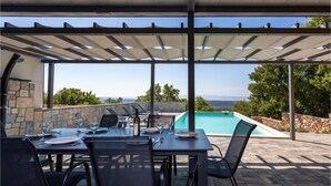 Un espace extérieur aménagé pour les repas, avec une piscine, des murs en pierre et une vue sur l’océan.