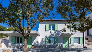 Un bâtiment à deux étages avec des volets verts, des fondations en pierre et un ciel bleu clair en arrière-plan.