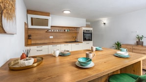 Une cuisine moderne avec des armoires blanches, un plan de travail en bois et un four encastré. On y trouve divers ustensiles de cuisine et une plante en pot sur le plan de travail.