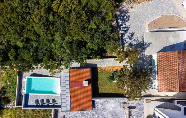 An aerial view of a residential area with a swimming pool, a red-roofed structure, and a paved driveway.