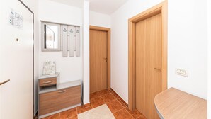 Un pasillo con pared blanca, puerta de madera, un espejo y una mesita.