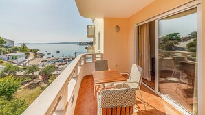 Un balcón con una mesa y sillas, con vista a un puerto deportivo con barcos y una costa lejana.