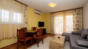 Una sala de estar con una mesa de centro de madera, un sofá gris, un televisor y una mesa de comedor con sillas.