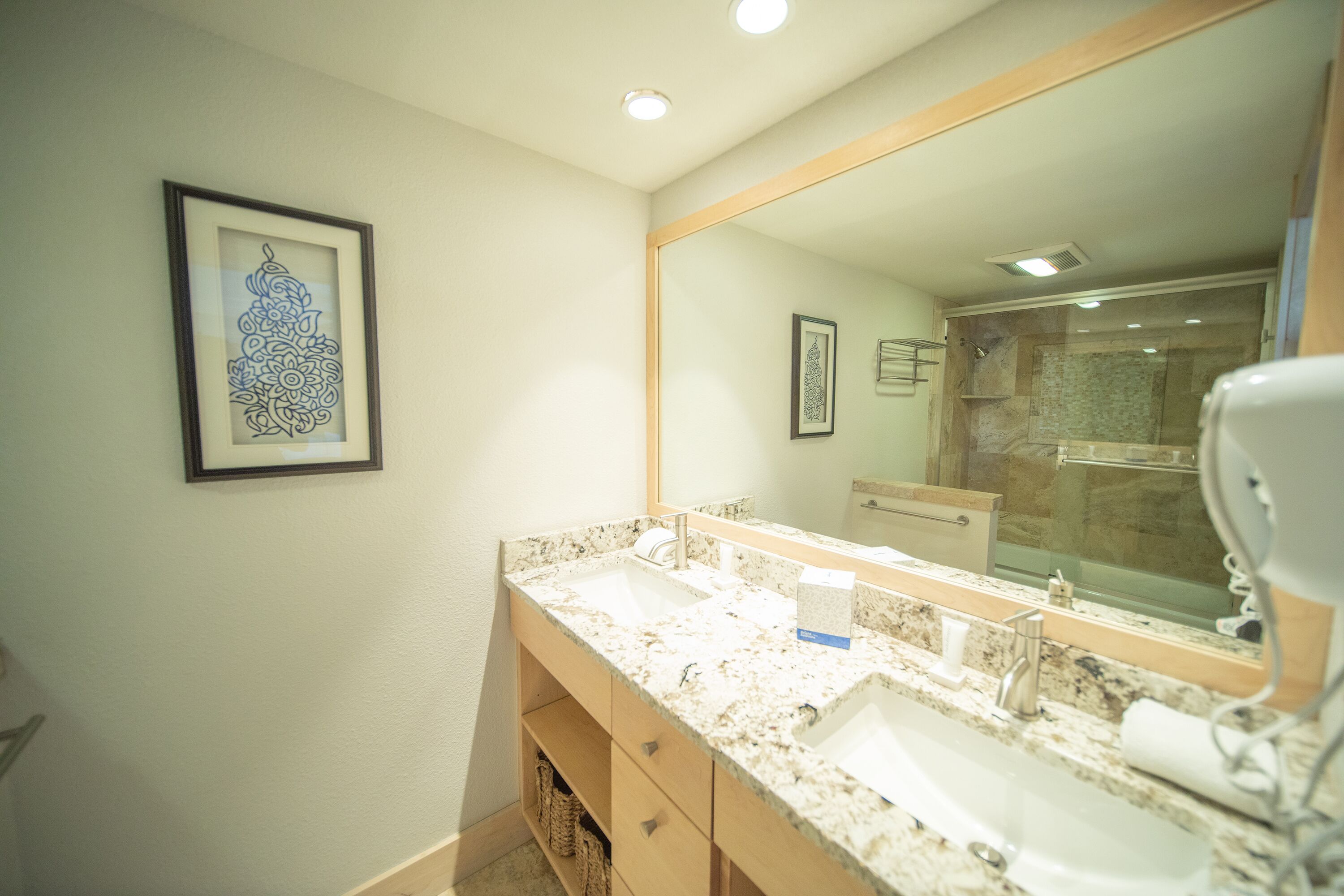 Un baño con un espejo grande, dos lavamanos y una obra de arte enmarcada en la pared.
