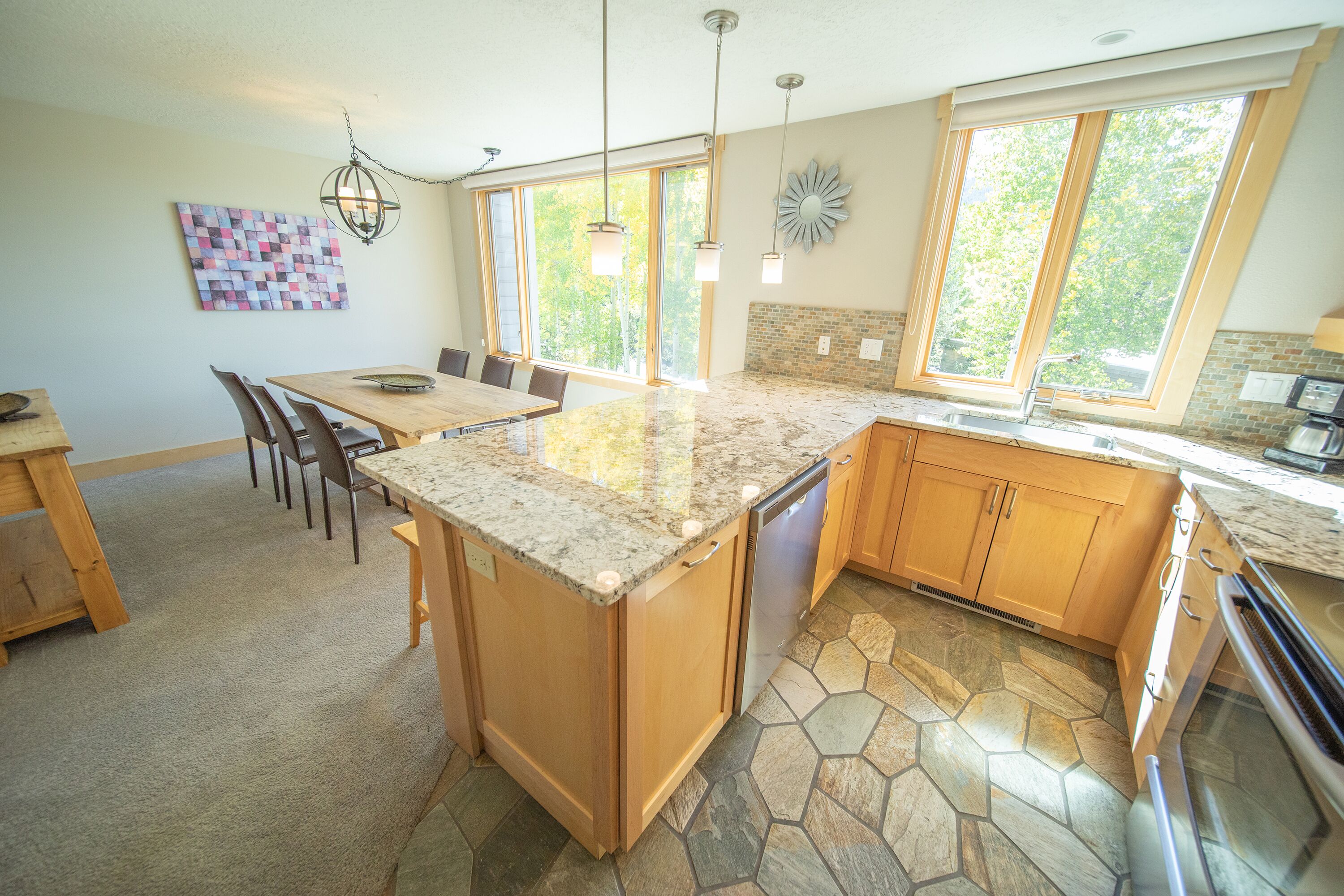A kitchen with a large island, wooden cabinets, a stone backsplash, and a dining area with chairs.