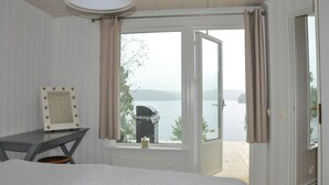 A bedroom with a bed, a vanity with a mirror, and a view of a lake through an open door. - Lovely home in Färgelanda with sauna (Färgelanda)