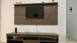 En moderne stue med et vægmonteret fladskærms-tv, en træunderholdningsenhed og en lille potteplante på væggen.