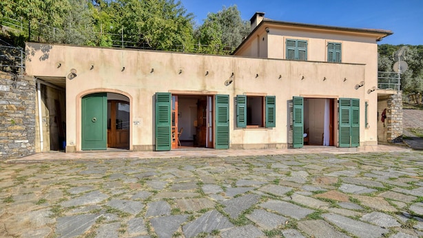 Un bâtiment à deux étages doté d’une cour pavée de pierres, de volets verts et d’un mur de pierre sur l’un de ses côtés.