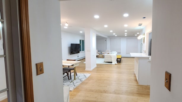 Un intérieur moderne avec un plancher en bois, des murs blancs, un coin repas avec une table et des chaises, un canapé et un téléviseur fixé au mur.