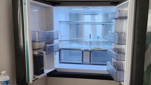 Un réfrigérateur ouvert, doté de plusieurs étagères et compartiments, d’un distributeur d’eau et d’un four à micro-ondes.