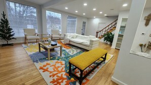 Un salon moderne avec un canapé blanc, deux fauteuils, une table basse et un banc. On y trouve un petit sapin de Noël et un escalier menant à un autre niveau.