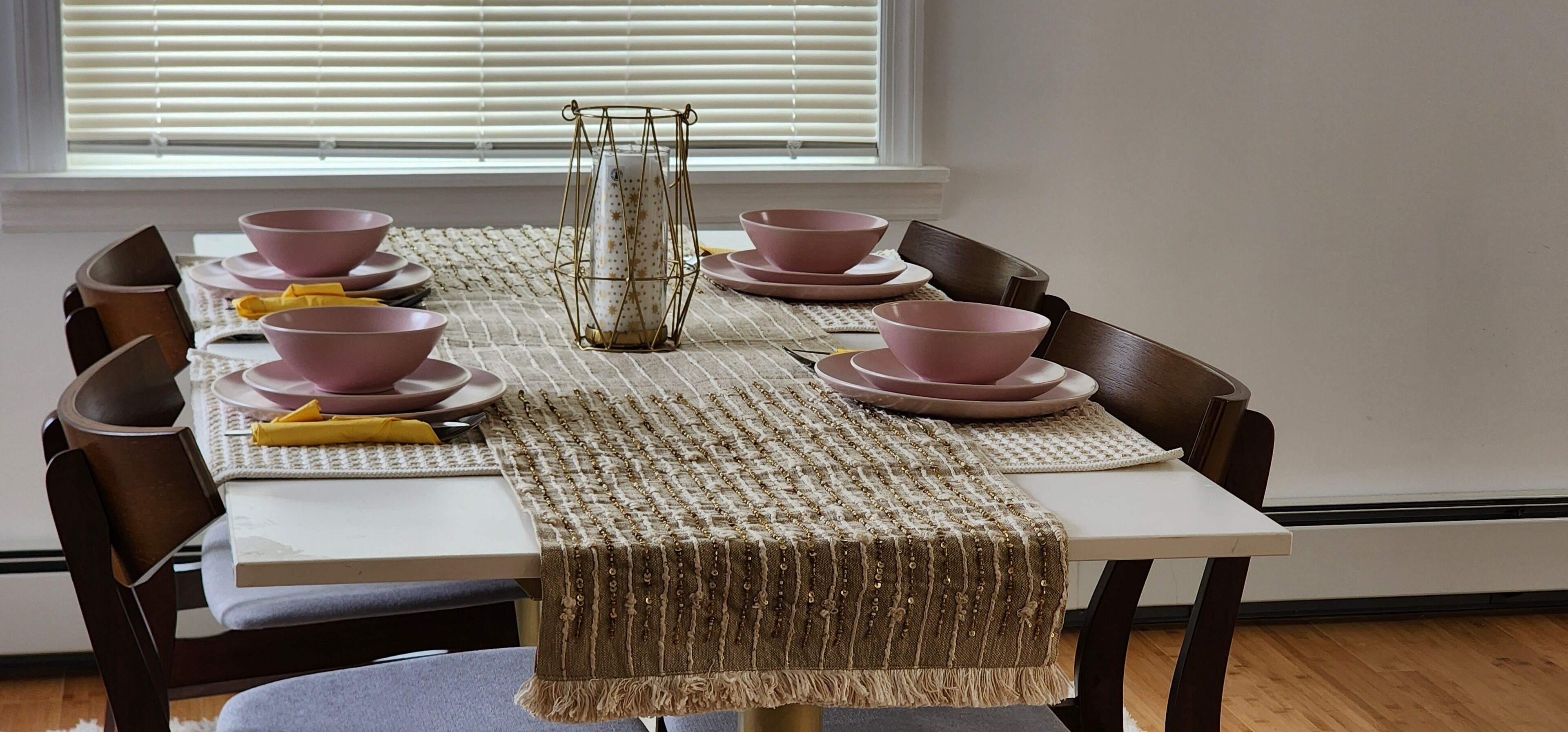 A dining table set with pink bowls and plates, a woven placemat, and a decorative candle holder.