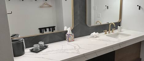A modern bathroom with a white marble countertop, dual sinks, and a large mirror with gold-framed lights.
