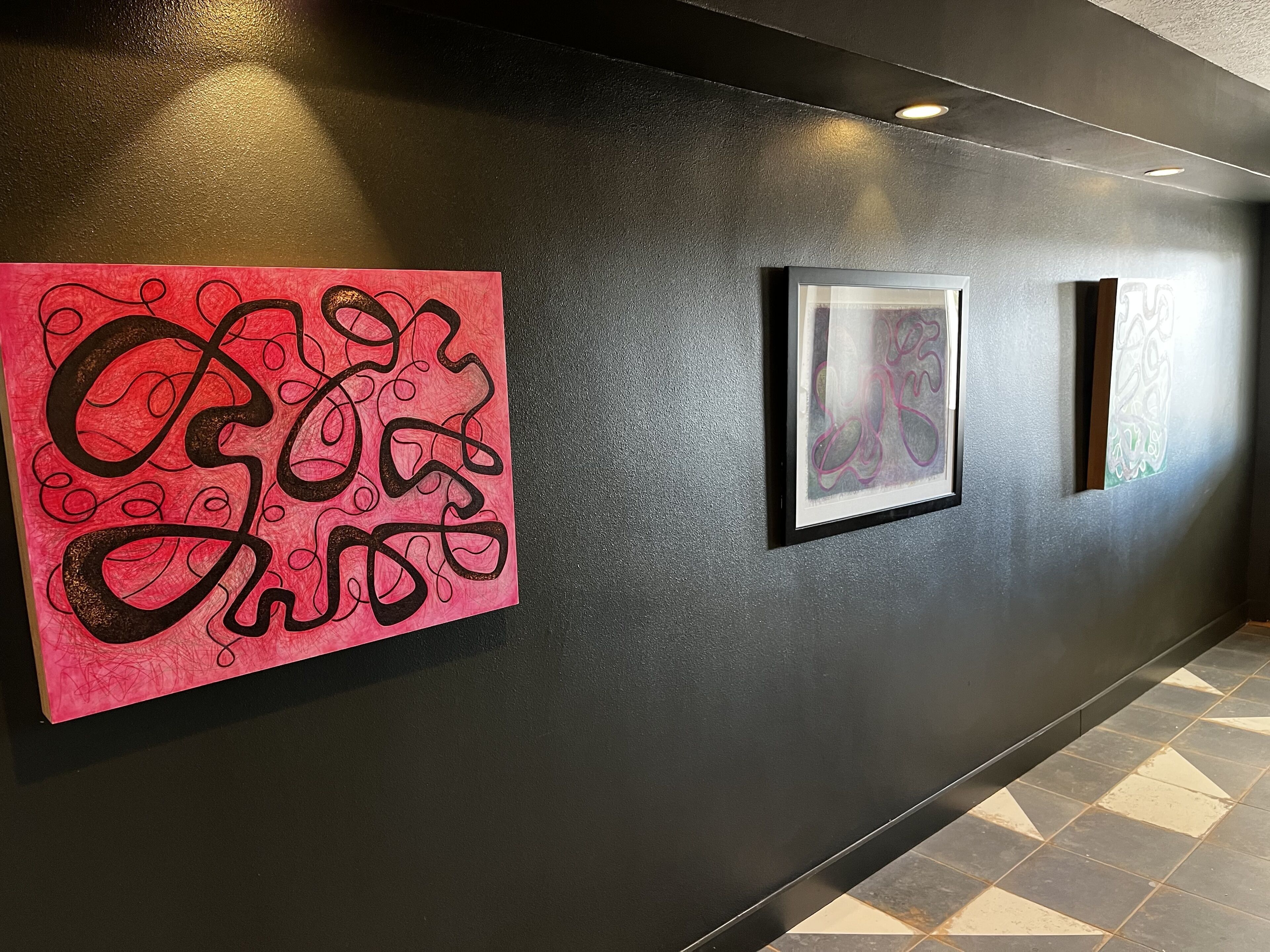 A hallway with a black wall and a large abstract painting on the left.