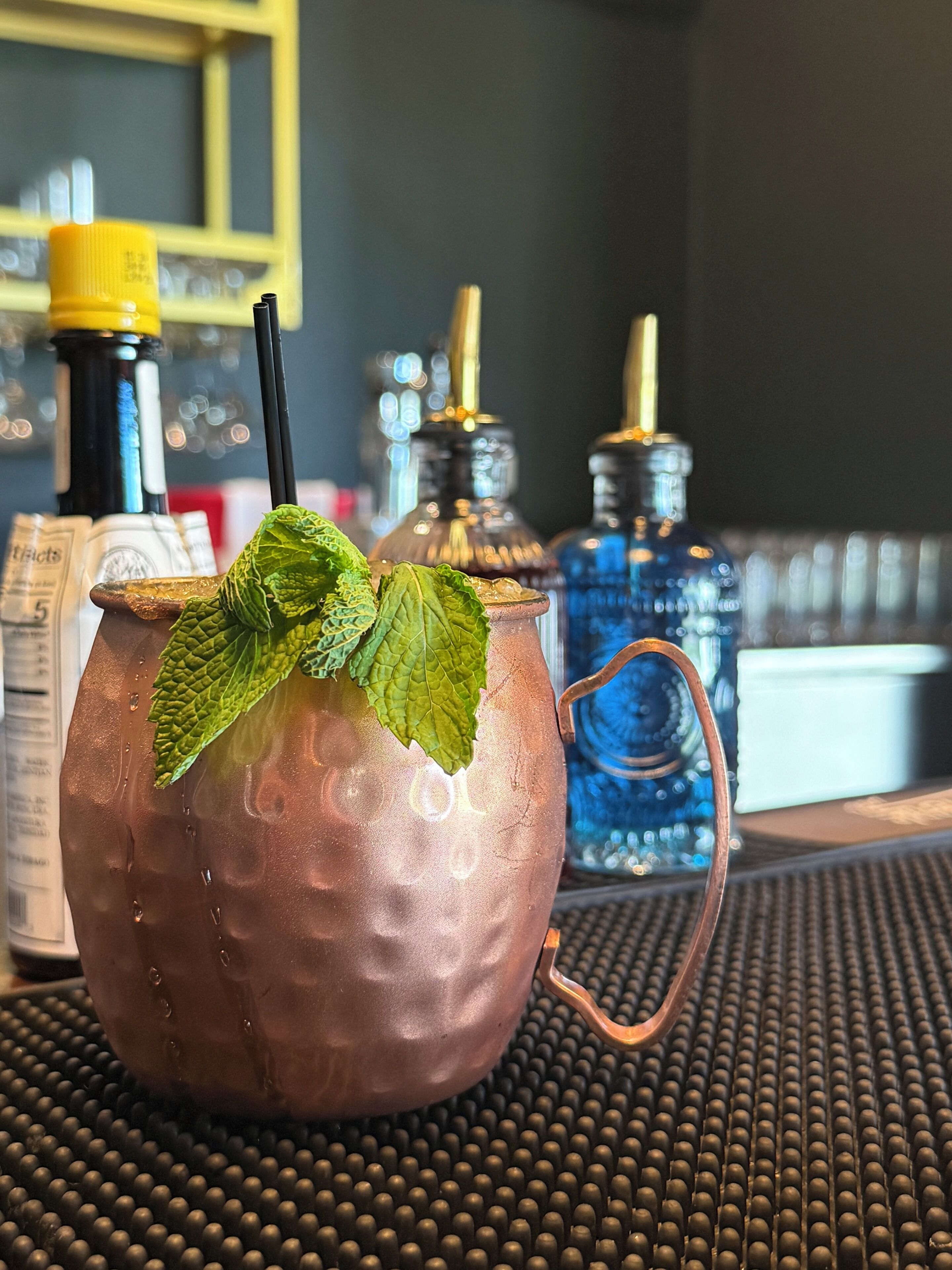 A copper mug with a handle and a green leaf garnish, placed on a textured surface.