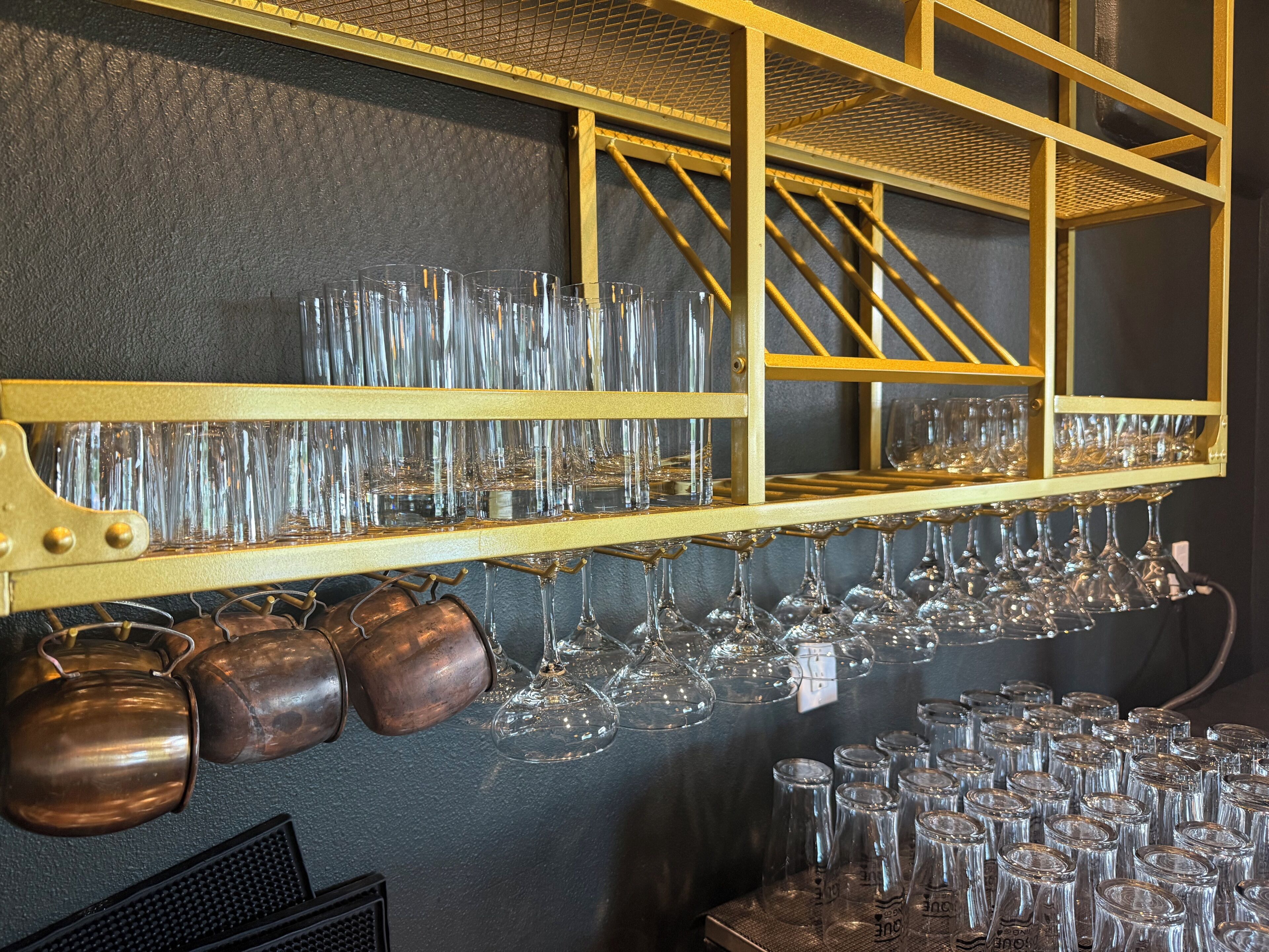 A bar area with shelves holding multiple glasses and copper mugs.