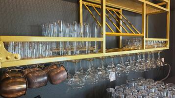 A bar area with shelves holding multiple glasses and copper mugs.