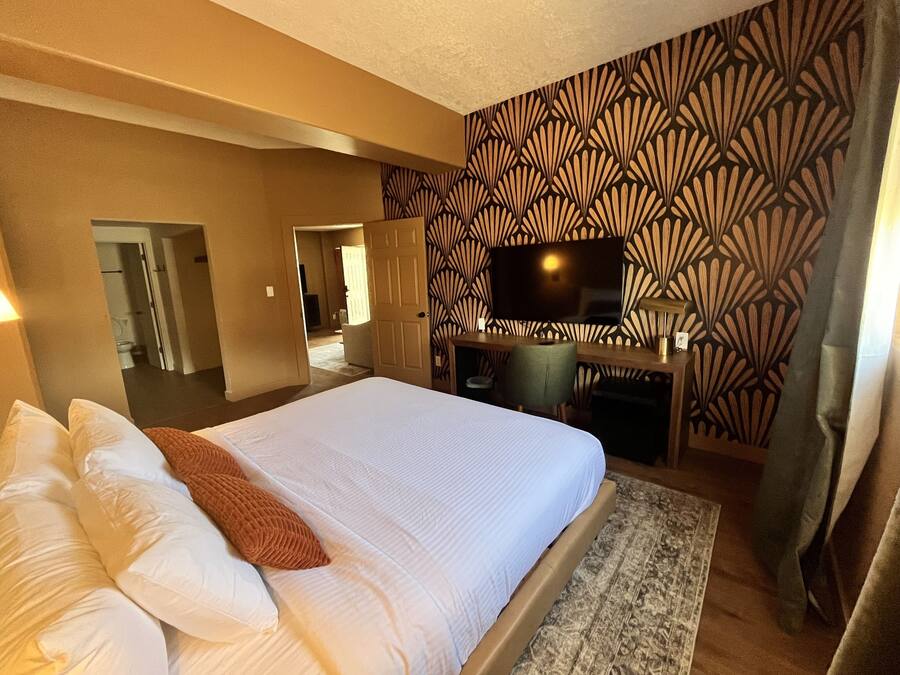 A hotel room with a large bed, a desk, a TV, and a patterned wall.