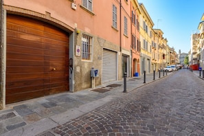 Una calle adoquinada flanqueada por edificios históricos, una puerta de madera cerrada y una señal de 'prohibido estacionar'.