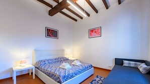 Un dormitorio con cama, mesitas de noche, un sofá y dos cuadros enmarcados en las paredes.