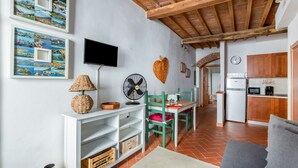 A living room with a TV, a fan, a heart-shaped decoration, and a dining area with chairs and a table. - GuestHost - Boboli Gardens Lovely Apartment (Firenze)