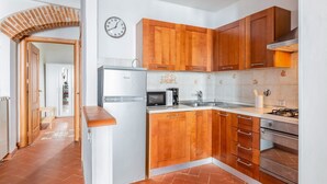 A kitchen with wooden cabinets, a microwave, a stove, and a clock on the wall. - GuestHost - Boboli Gardens Lovely Apartment (Firenze)