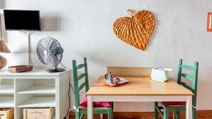 A room with a wooden table, green chairs, a white shelf, a wall-mounted TV, a fan, and a heart-shaped decoration. - GuestHost - Boboli Gardens Lovely Apartment (Firenze)
