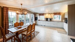 Een ruime keuken met houten kastjes, een eethoek met een houten tafel en stoelen, en grote ramen die zorgen voor veel daglicht.