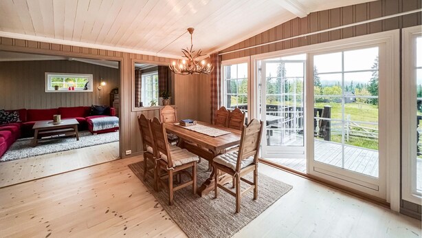 Een ruime woonkamer met een houten eettafel, een rode bank en een grote glazen schuifdeur die leidt naar een terras.