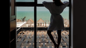 A room with a large window overlooking a beach with umbrellas and lounge chairs.