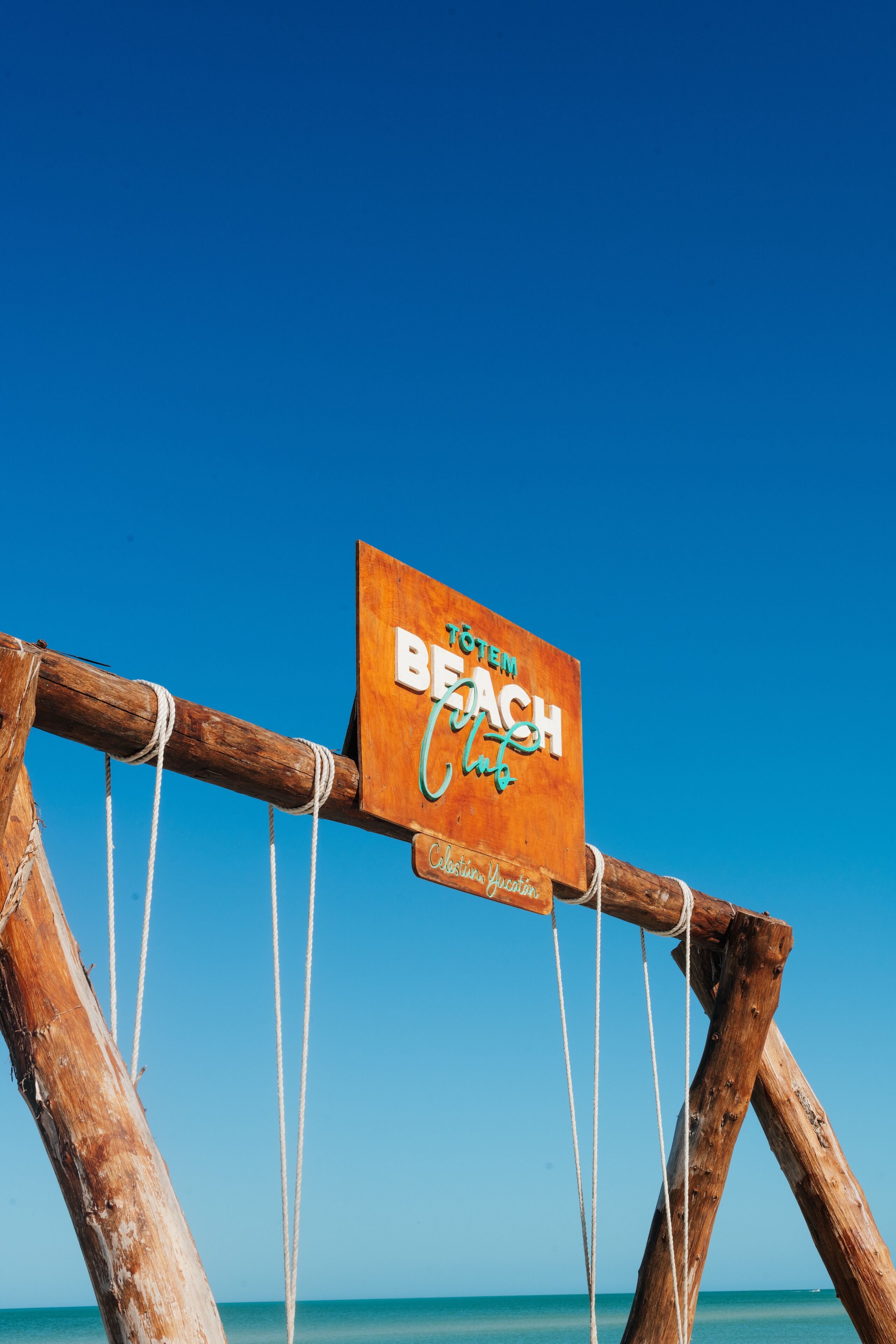Une enseigne en bois portant l’inscription « BREATHE BEACH » et « Casanova Bay », sur fond de ciel bleu clair.