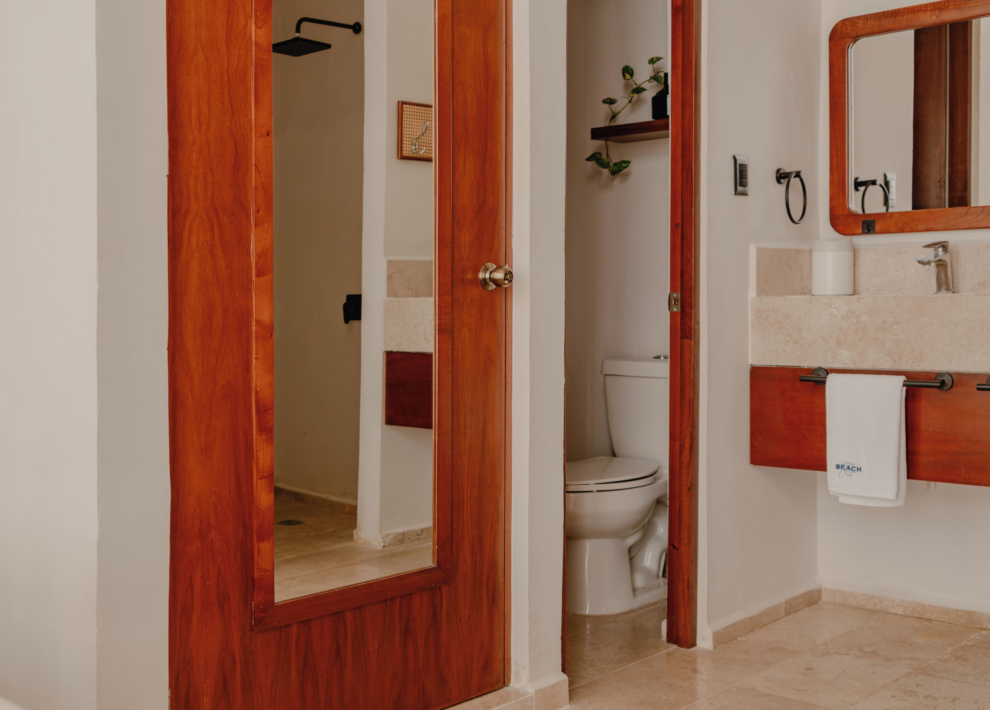 Een badkamer met een houten deur, een toilet, een wastafel met spiegel en een handdoekrek.