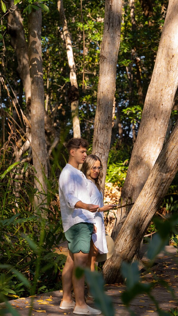 Una pareja de pie en una zona boscosa con árboles y follaje al fondo.