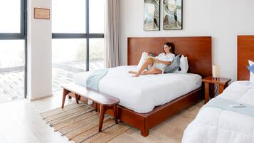 Un dormitorio moderno con una cama grande, una mesita de noche, un banco y vistas de la ciudad a través de amplios ventanales.