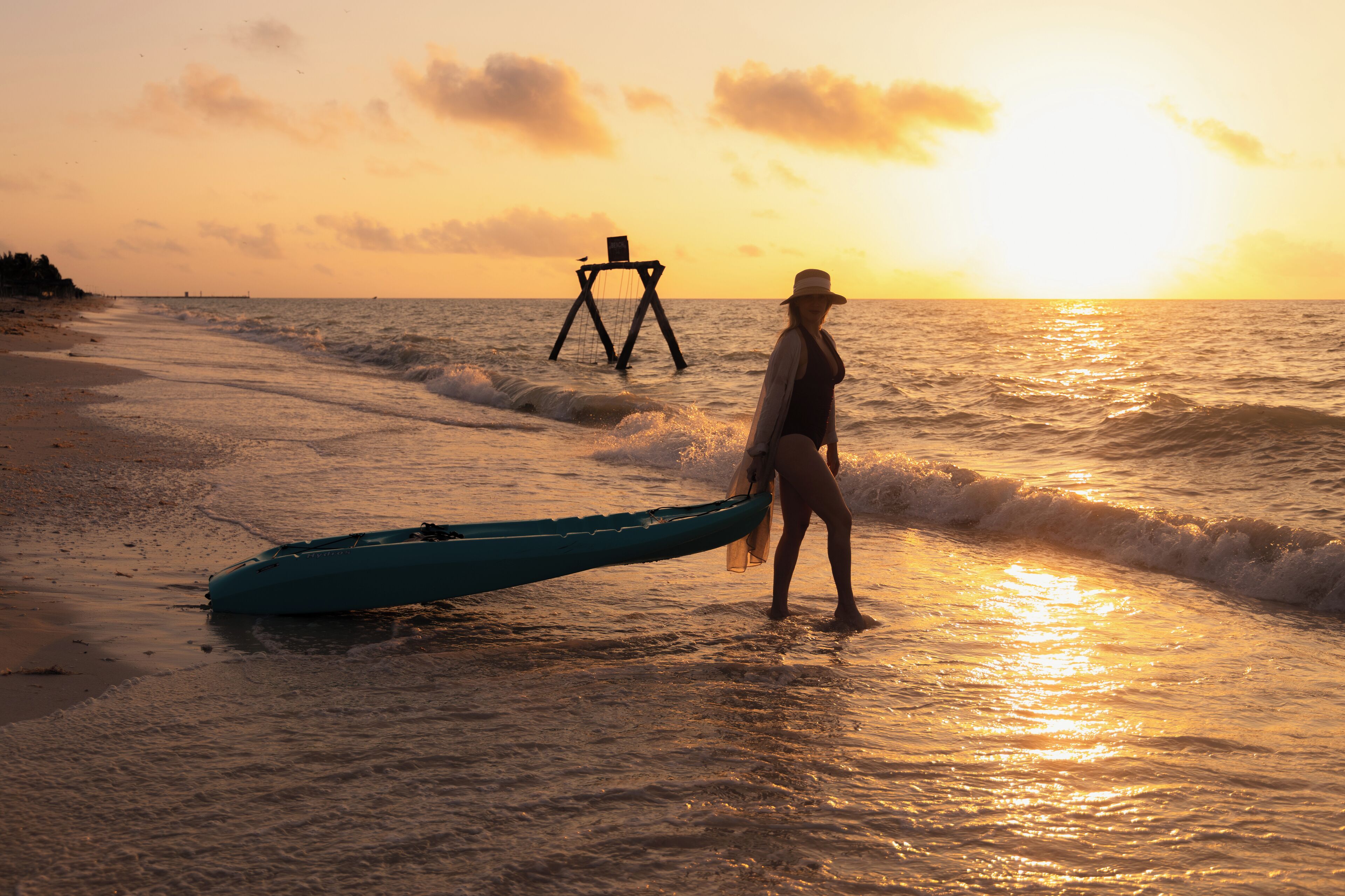 Escena de playa con una persona sosteniendo un kayak y un trípode en el agua.