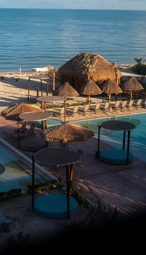 A beachside resort with a pool, lounge chairs, and thatched umbrellas.