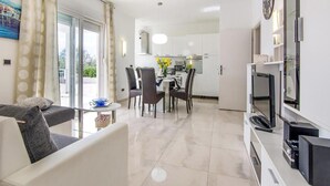 Un soggiorno moderno con divano, un'area pranzo con sedie e tavolo, una cucina con elettrodomestici e una TV su un mobile.