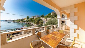 Un balcon doté d’une table en bois et de chaises en osier, offrant une vue sur une zone côtière avec des bâtiments et des bateaux.