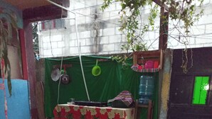 Un patio con una mesa cubierta con un mantel rojo y blanco, rodeado por un toldo verde. Hay recipientes de plástico y una silla cerca de la mesa.