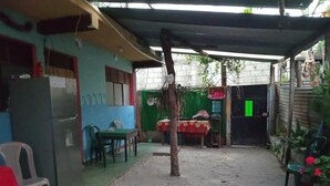 Un espacio exterior pequeño y cerrado con una mesa, sillas, refrigerador y una sección cubierta con pared verde.
