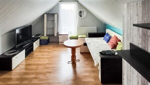 Un dormitorio estilo loft acogedor con piso de madera, una cama con almohadas coloridas, un televisor, una mesita y un ventanal con cortinas.