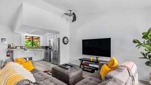 Un soggiorno moderno con un divano grigio, una televisione a schermo piatto e una cucina sullo sfondo.
