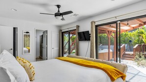Camera da letto moderna con un letto grande, una ventola a soffitto, una TV e vista sul patio esterno.