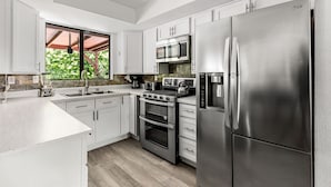 Una cucina moderna con mobili bianchi, elettrodomestici in acciaio inossidabile e un'ampia finestra che si affaccia sul verde.