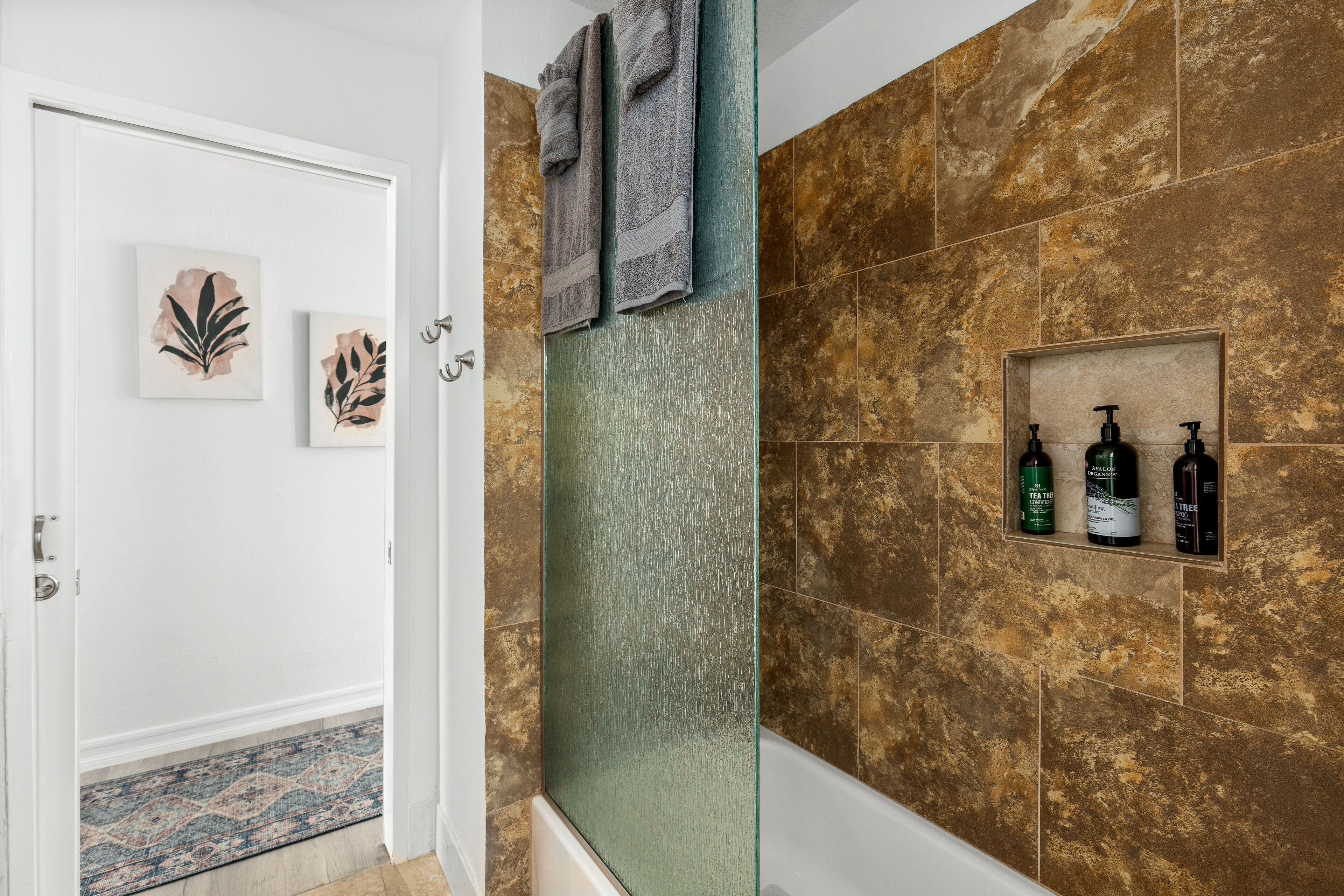 A bathroom with a shower area, a towel rack, and a shelf with toiletries.